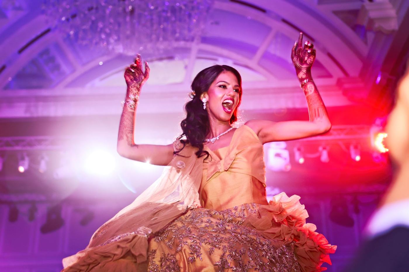 Bride dancing with her arms up in purple light