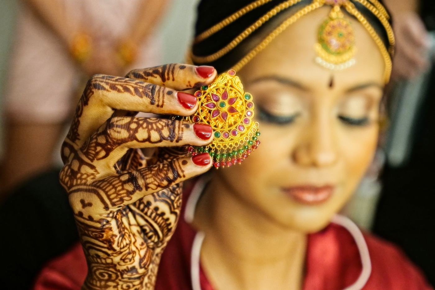 Bride holding her maang tikka in place with mehndi-covered hands