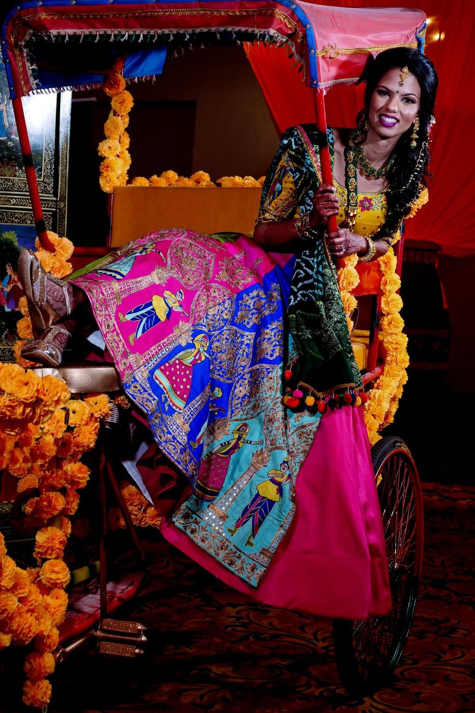 Bride laughing in a marigold-covered rickshaw at her sangeet