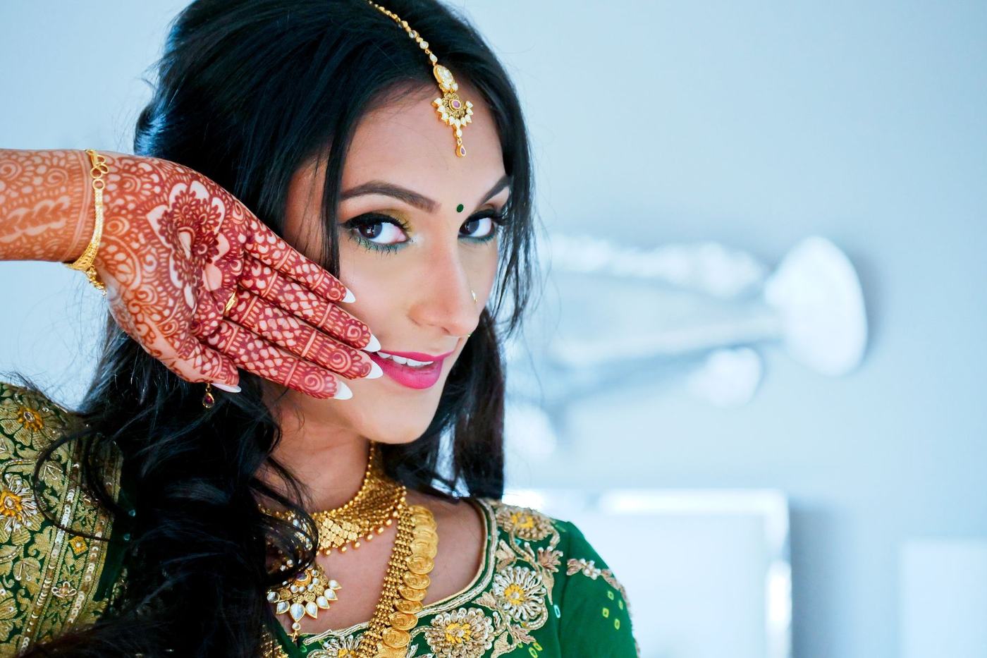 Bride in green showing her mehndi hand beside her face
