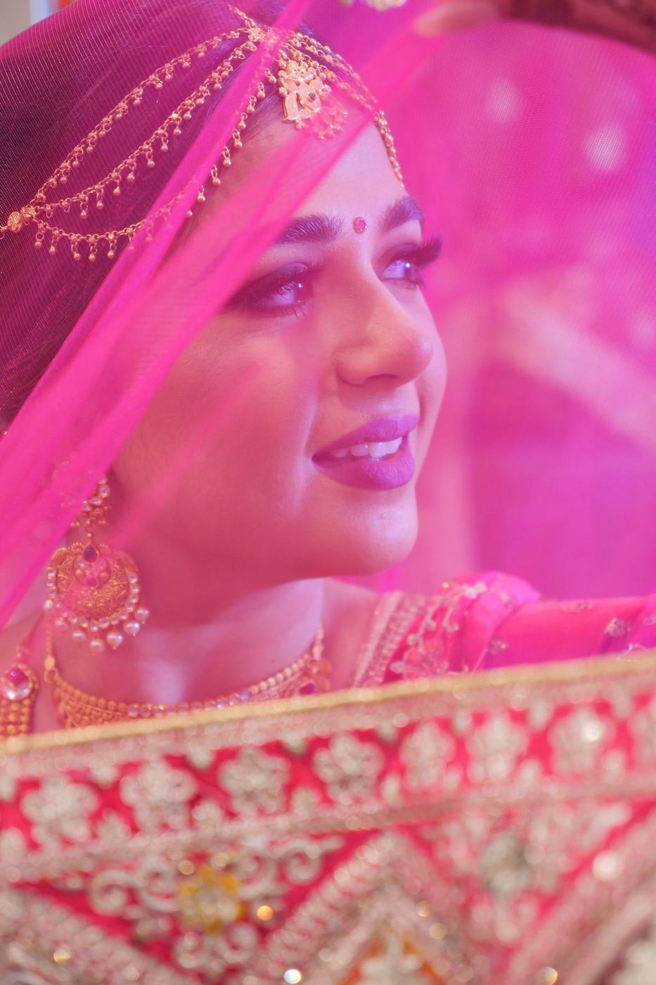 Bride in pink beneath a magenta veil, smiling