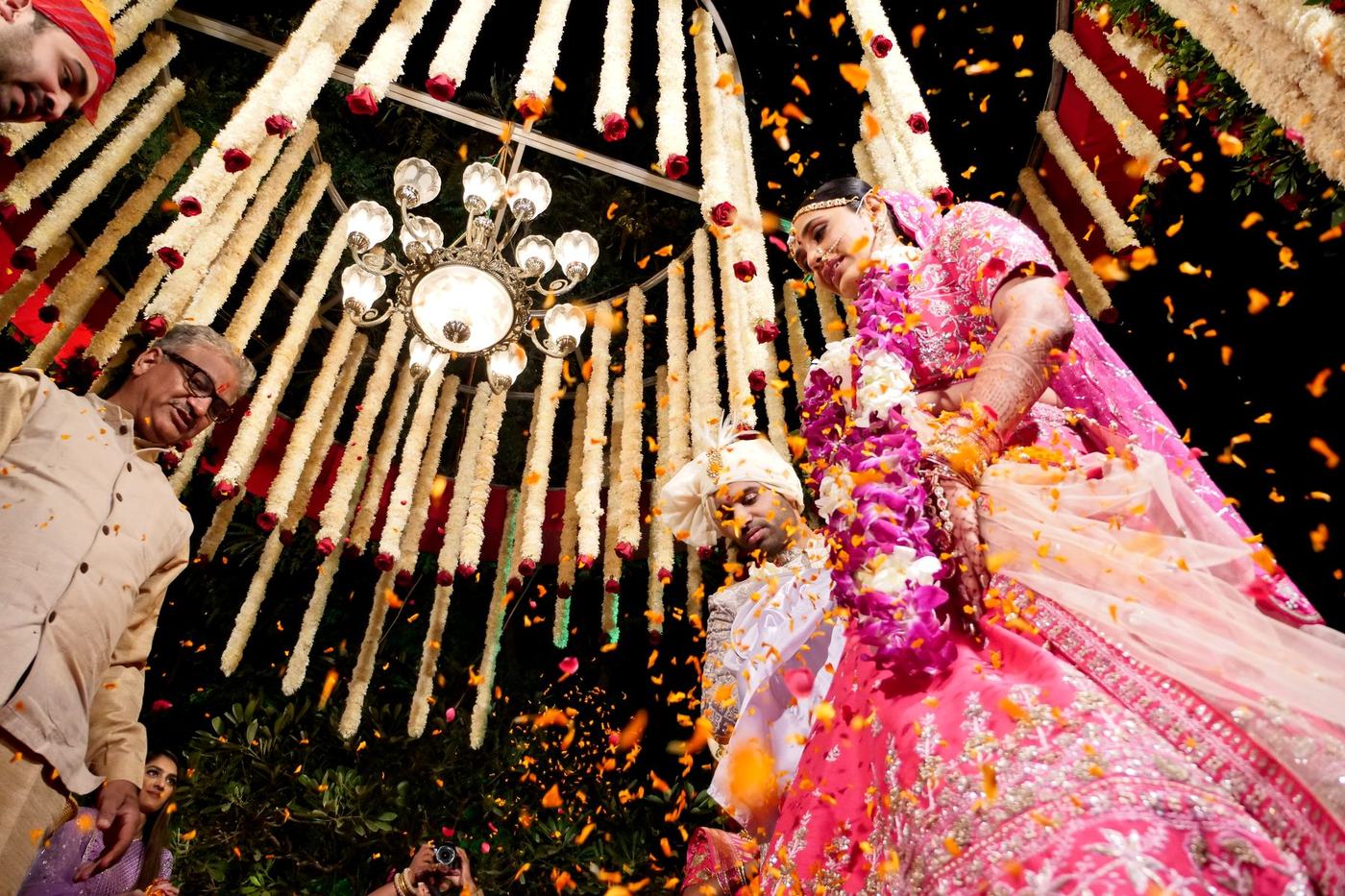 Bride in pink beneath a shower of petals and hanging marigold garlands