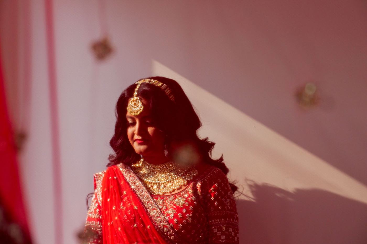 Bride beneath a red dupatta in soft pink light