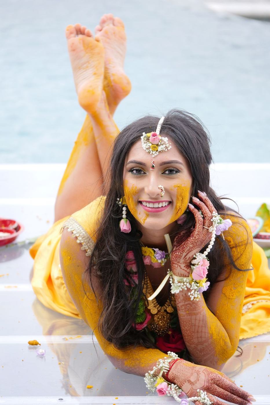 Bride in yellow lying by the pool at her haldi, feet in the air