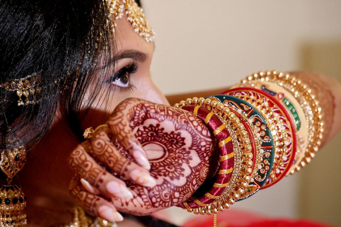 Bride lifting green and red bangles over her mehndi