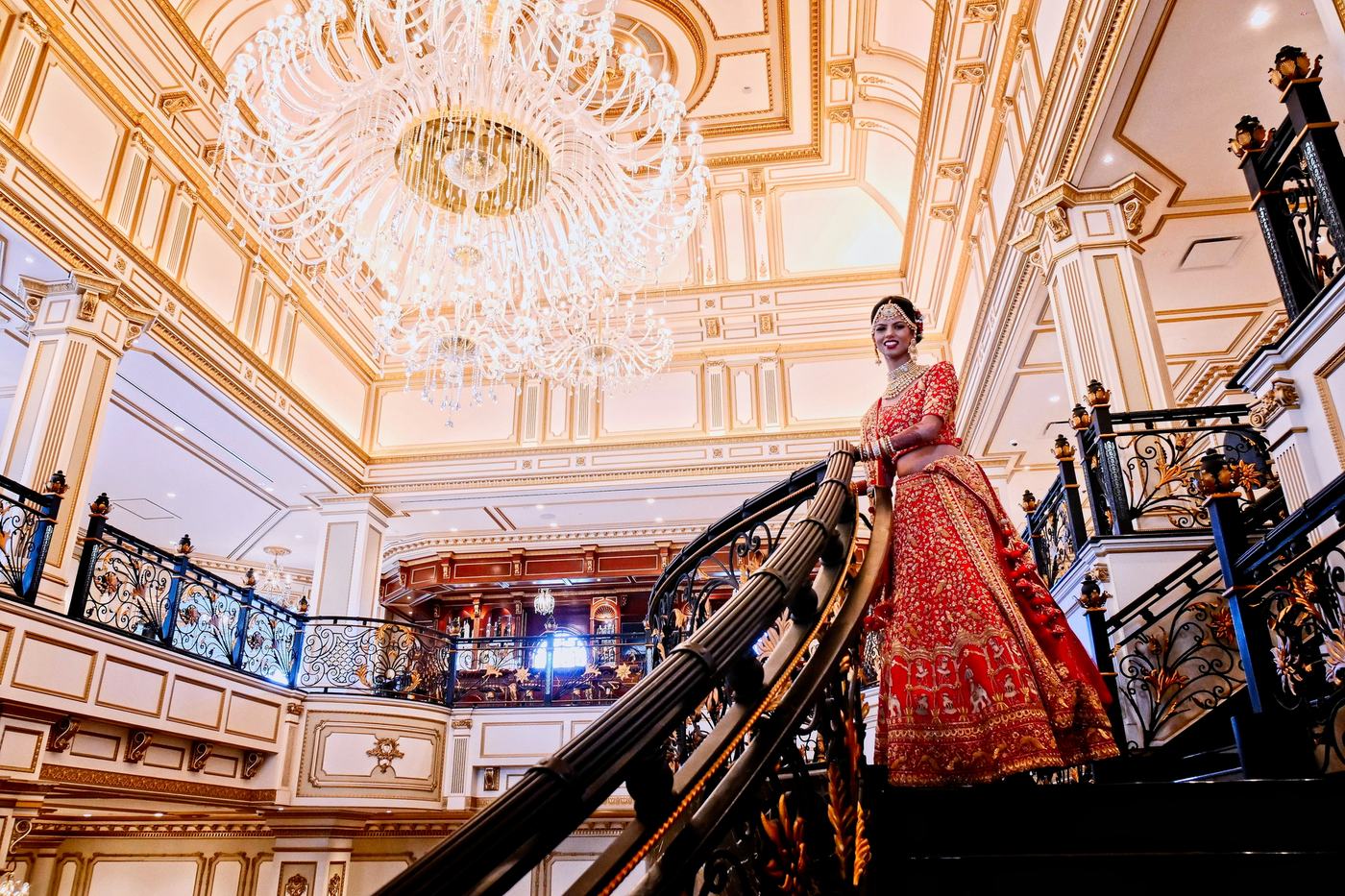 Bride on the grand staircase of The Legacy Castle beneath its chandelier