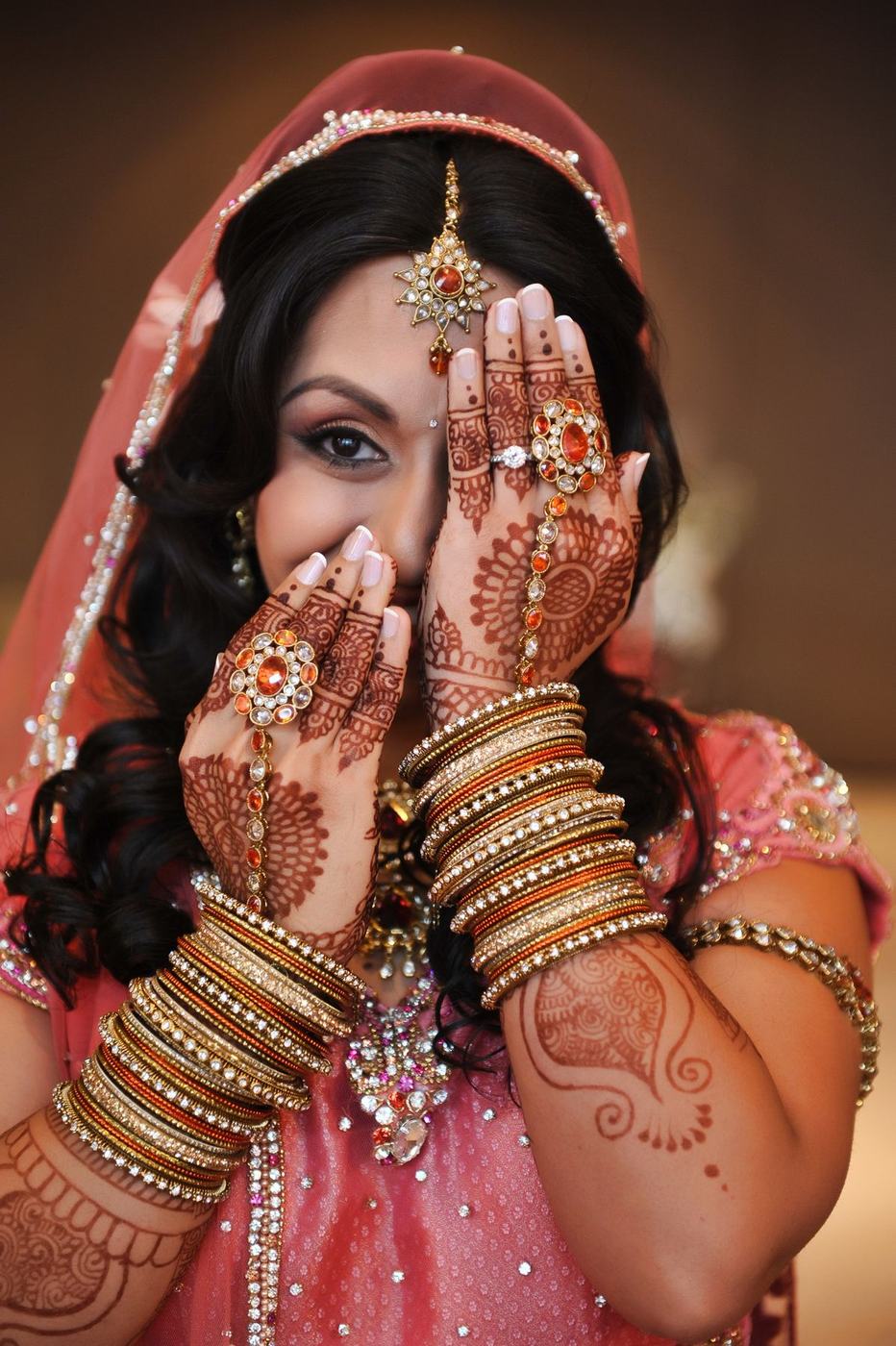Bride peeking through her mehndi-covered hands and bangles