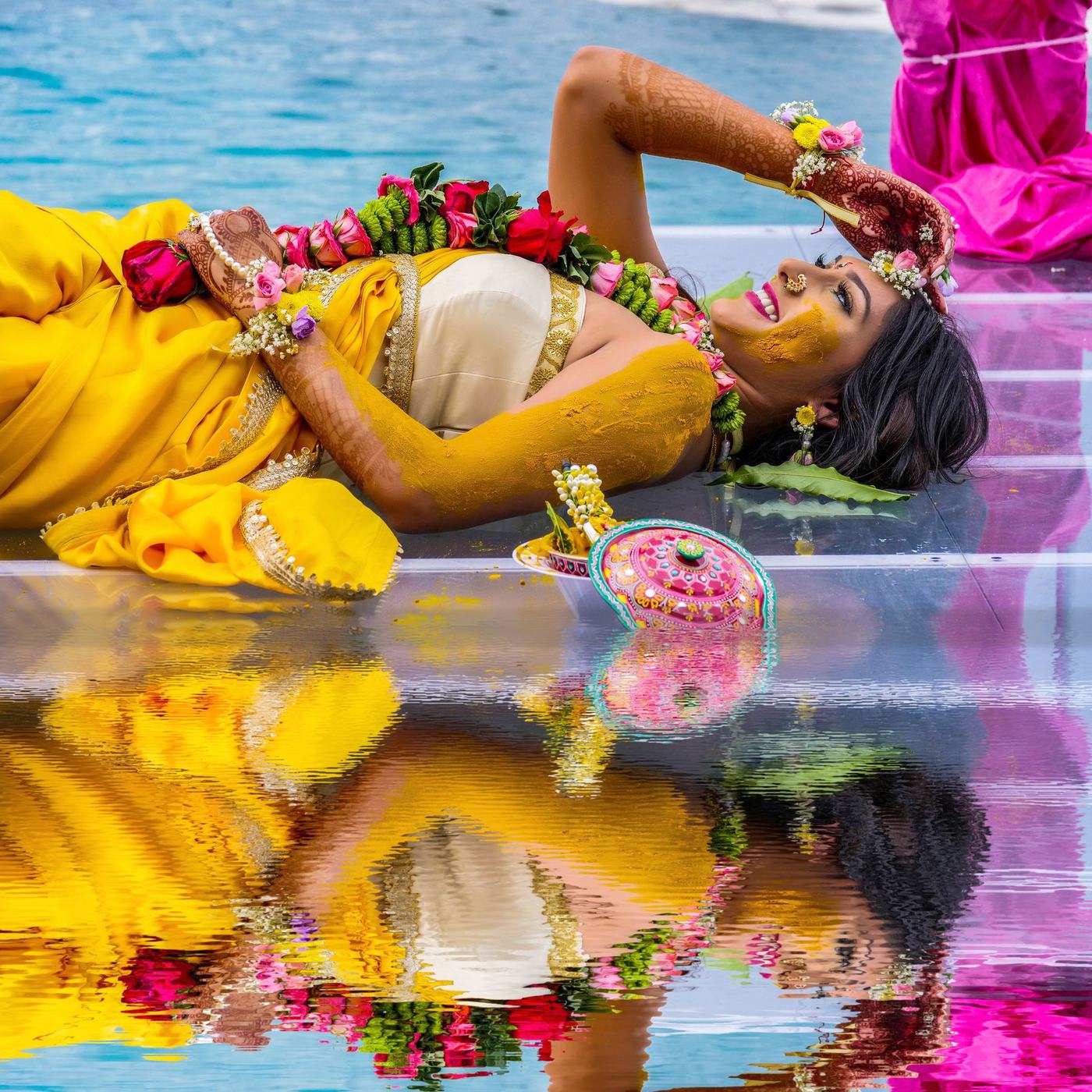 Bride in yellow reflected in the pool at her haldi