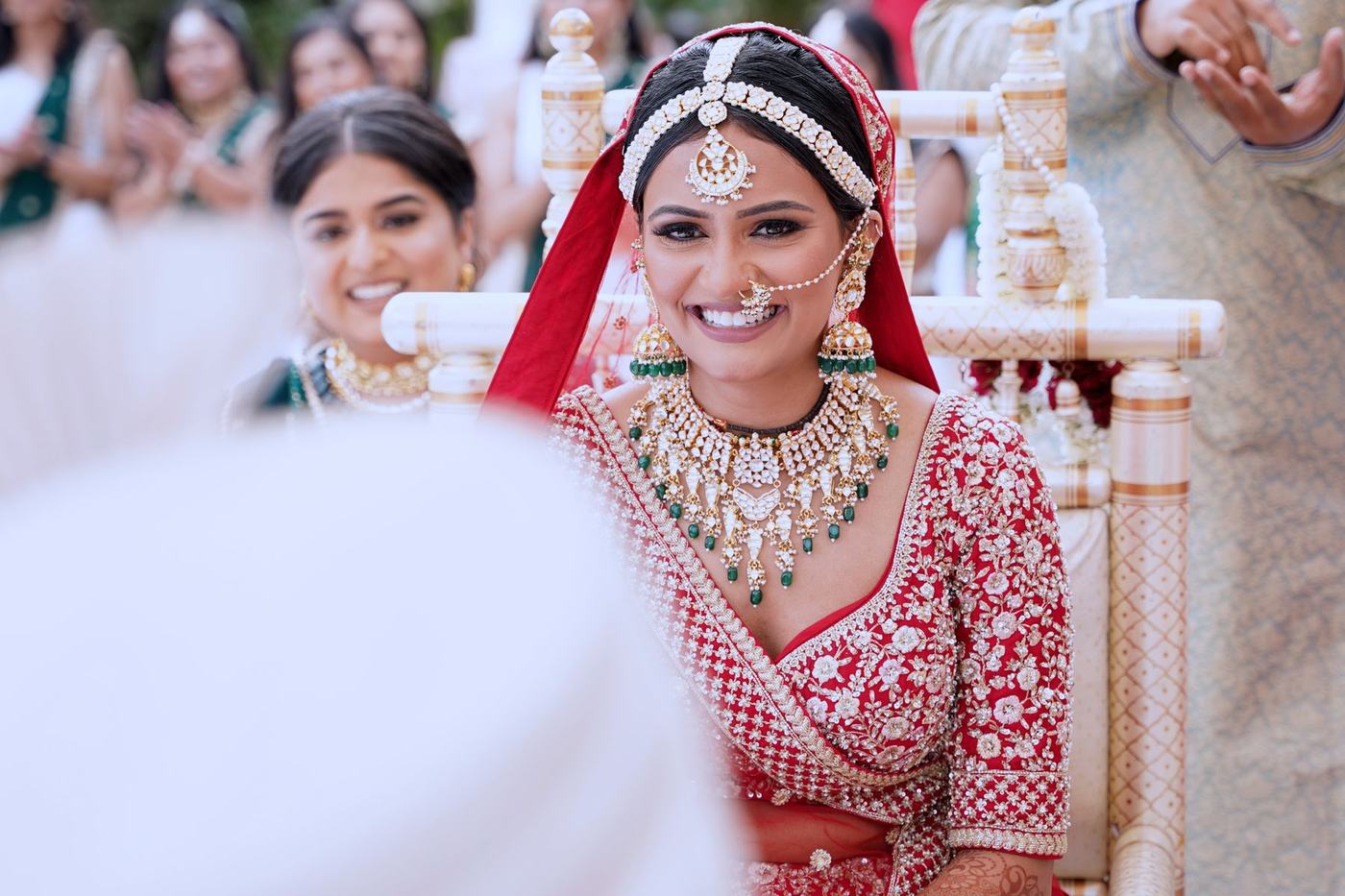 Bride smiling at the mandap in red and white with green jewels