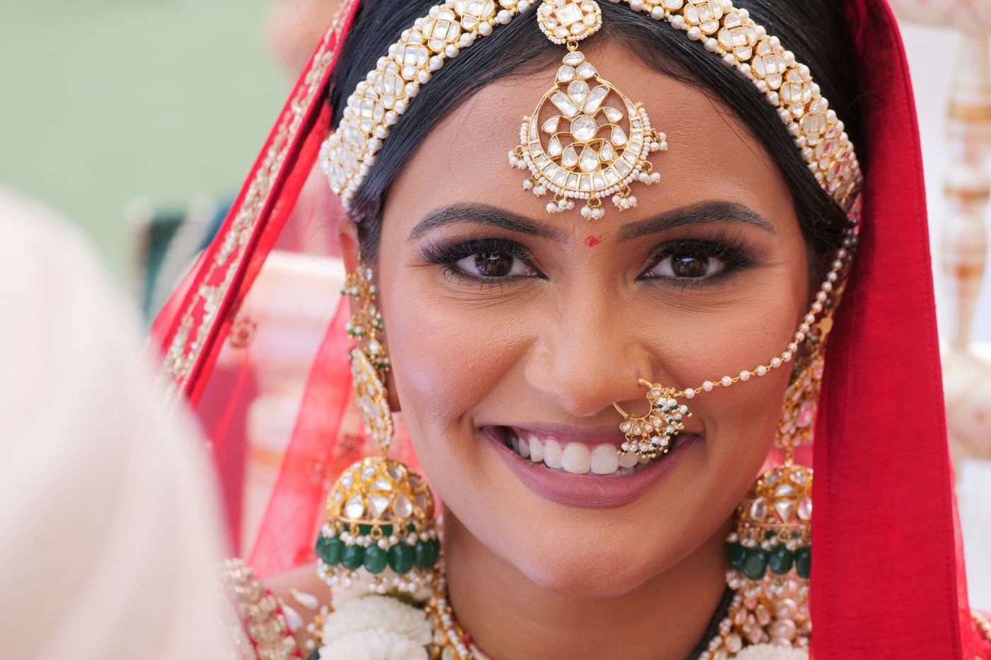 Bride smiling in red with emerald and kundan jewels