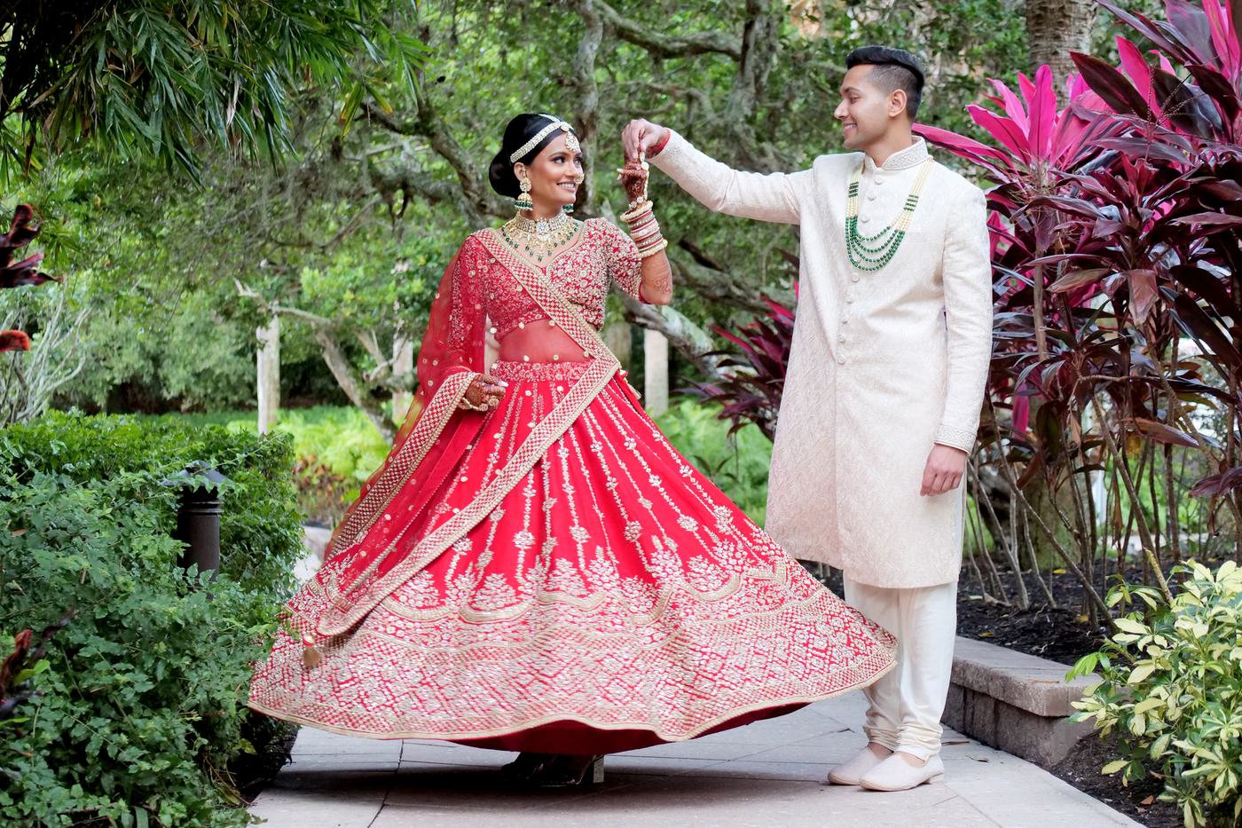 Groom spinning the bride so her red lehenga flares, in a Florida garden