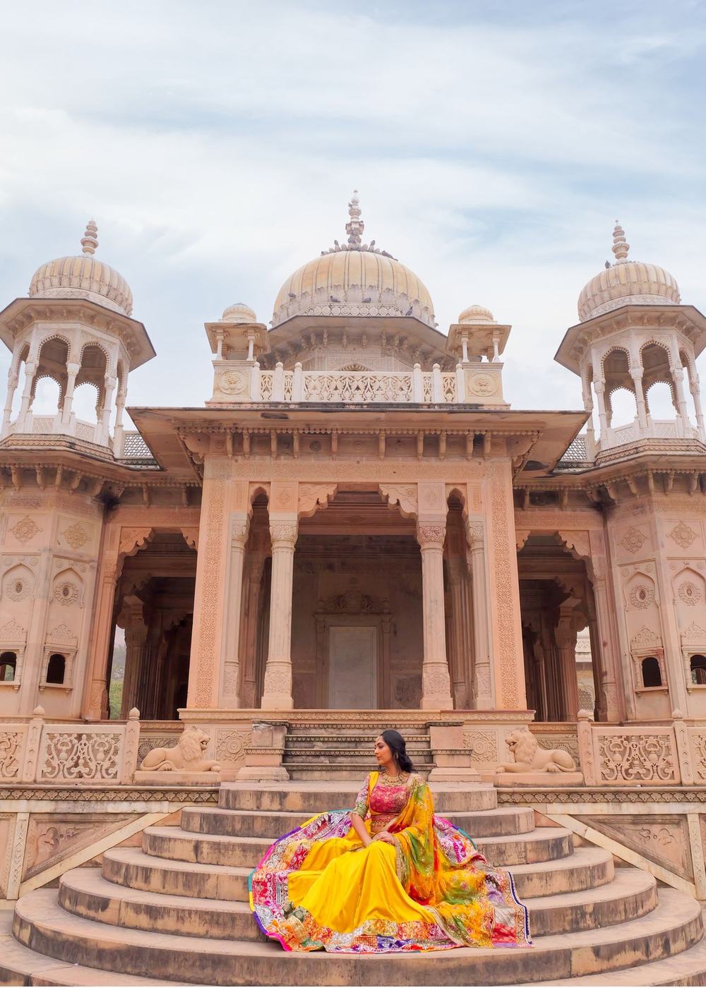 Bride in a yellow lehenga seated on the steps of a sandstone chhatri in Rajasthan
