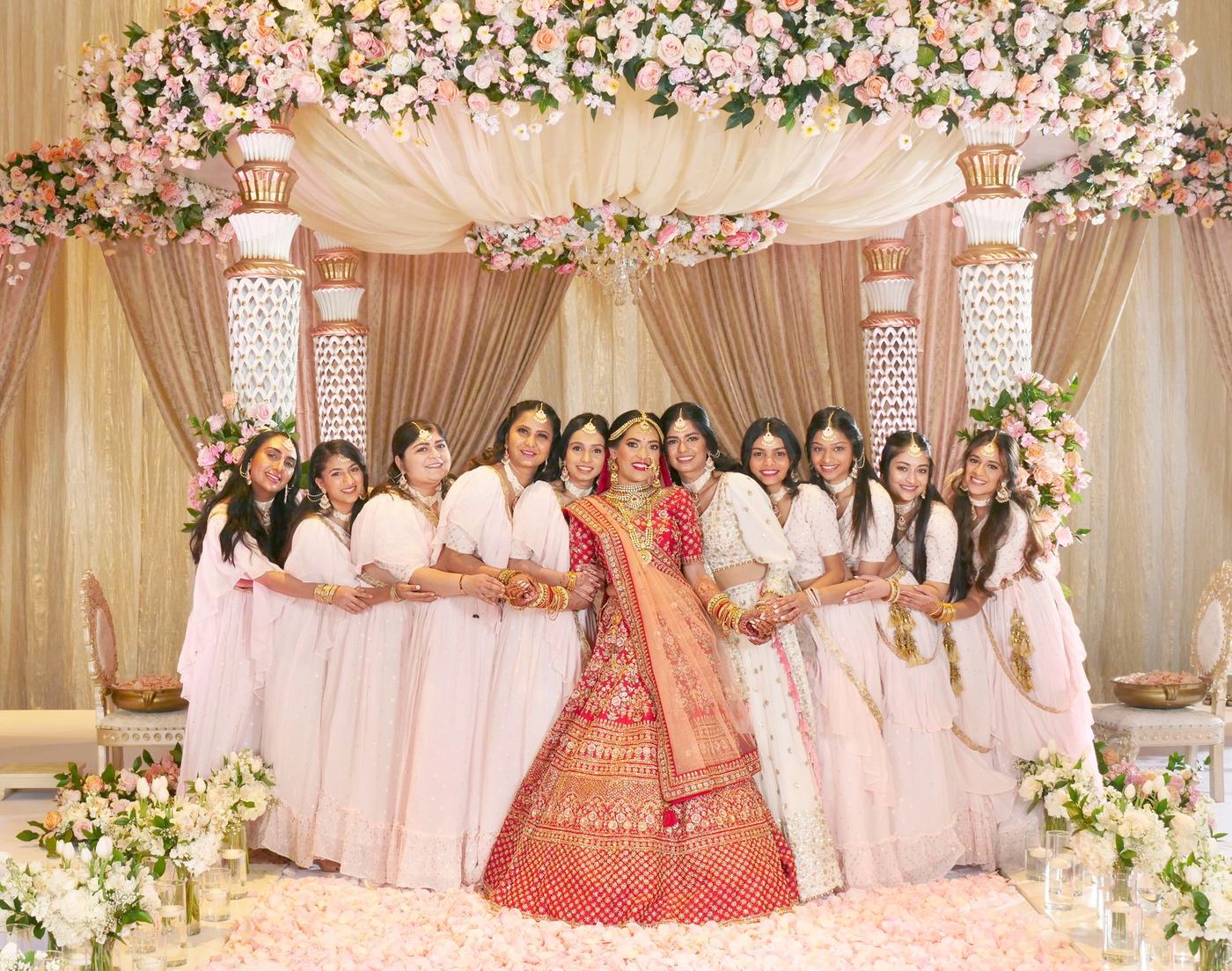 Bridesmaids in white around the bride at a mandap of blush florals