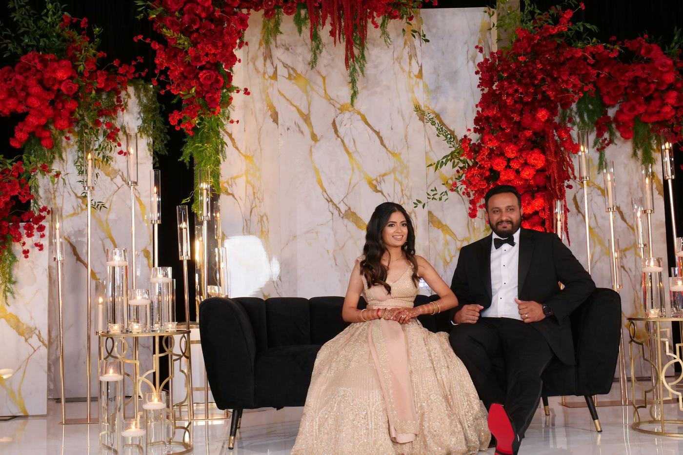 Couple seated on the marble reception stage beneath red roses