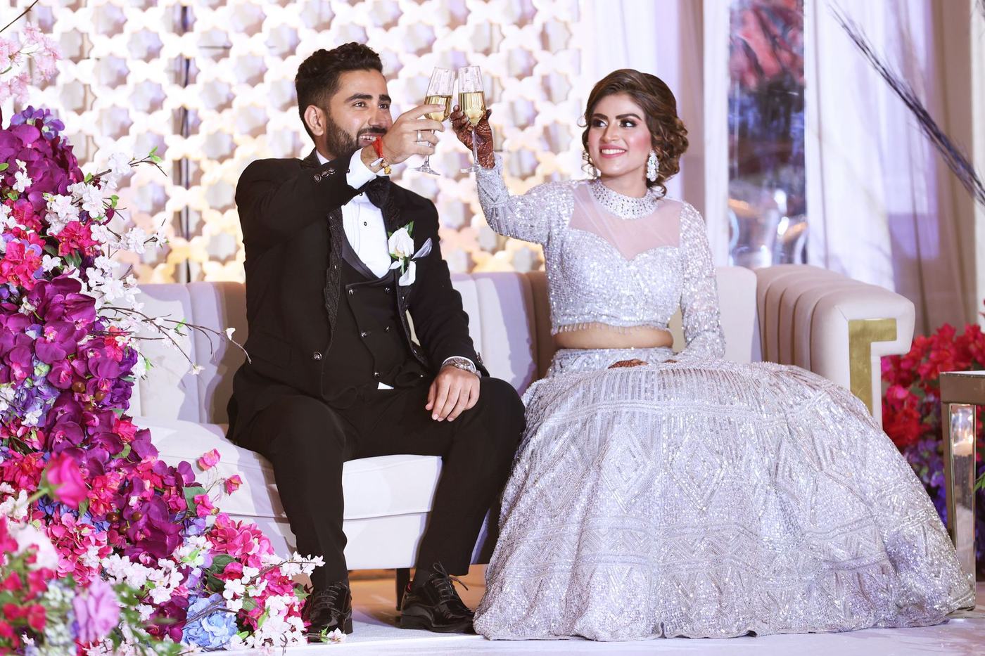 Couple raising a toast on a white sofa surrounded by pink reception florals