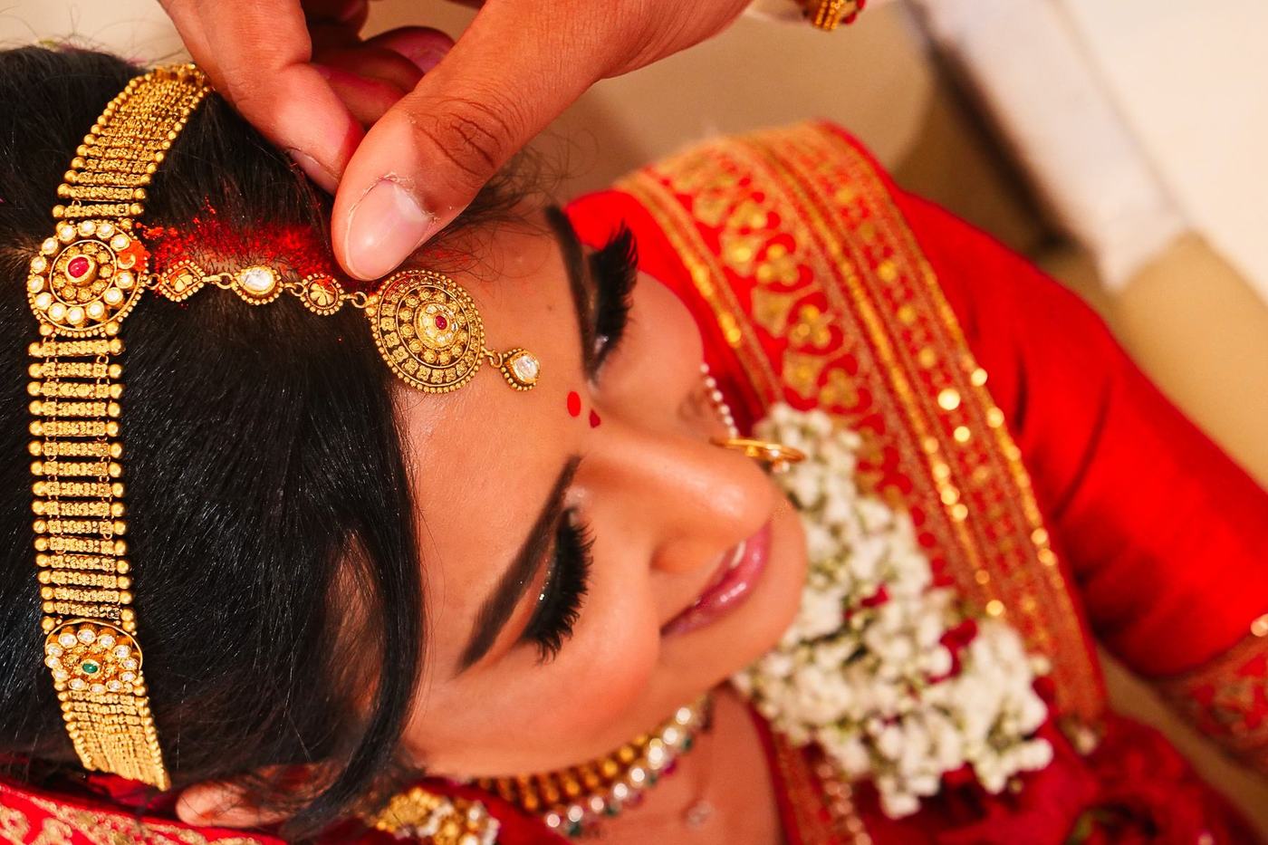 Fastening the gold maang tikka into the bride's hair