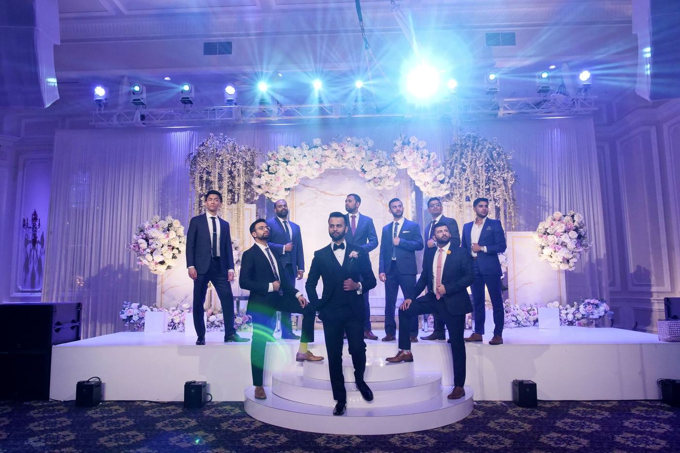 Groom and groomsmen in navy on the blue-lit reception stage