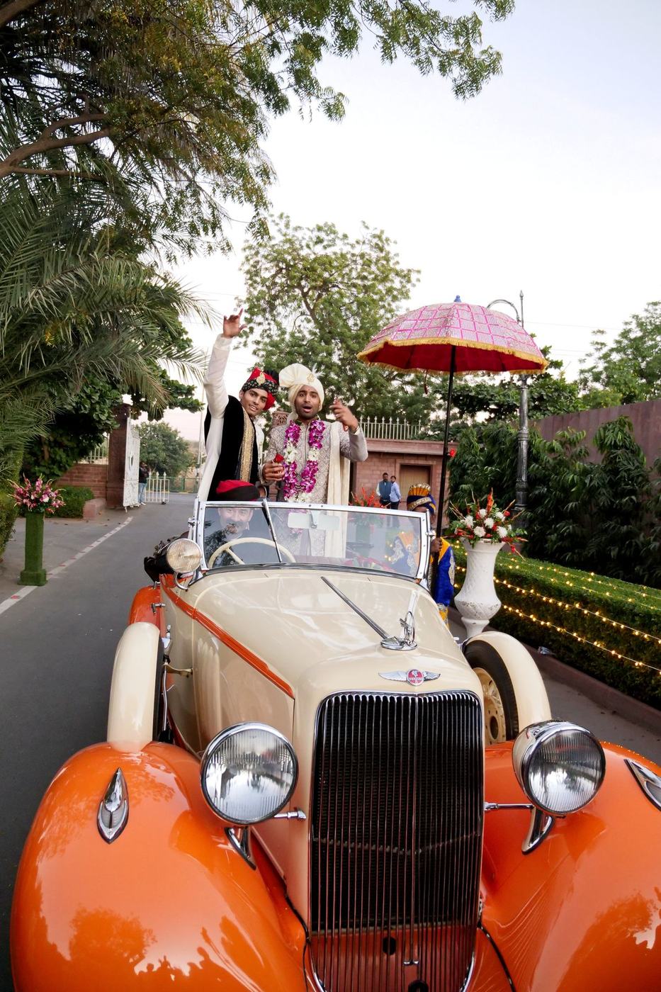 Groom arriving for his baraat in a vintage orange convertible