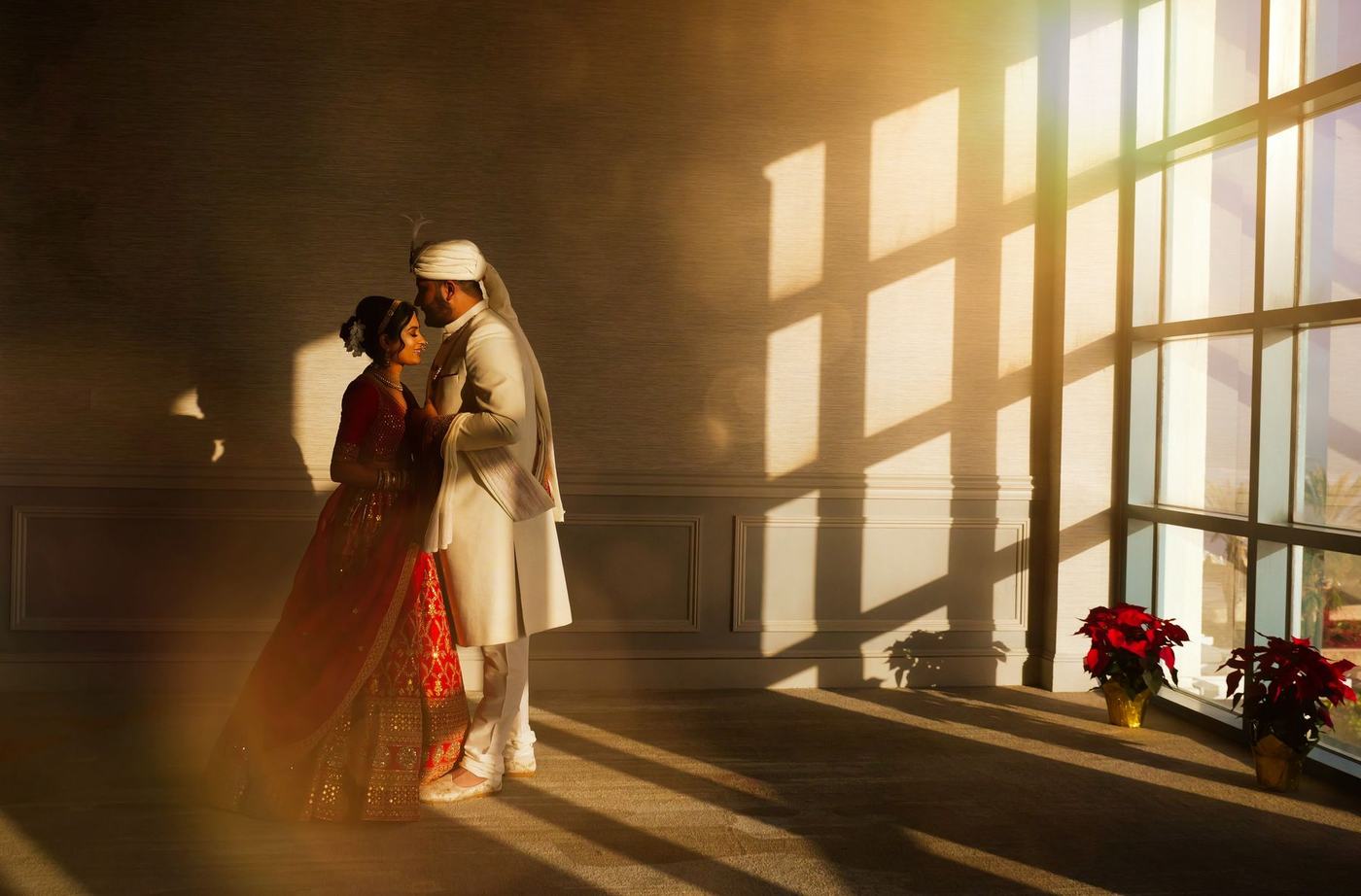 Groom kissing the bride in a tall sunlit window above the ocean