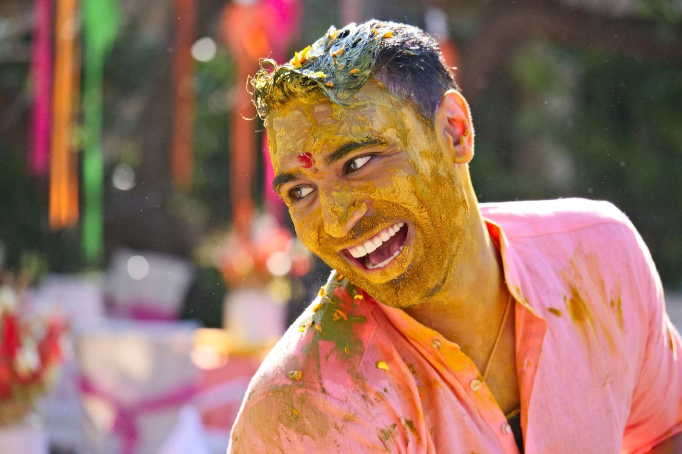 Groom laughing with his face covered in haldi