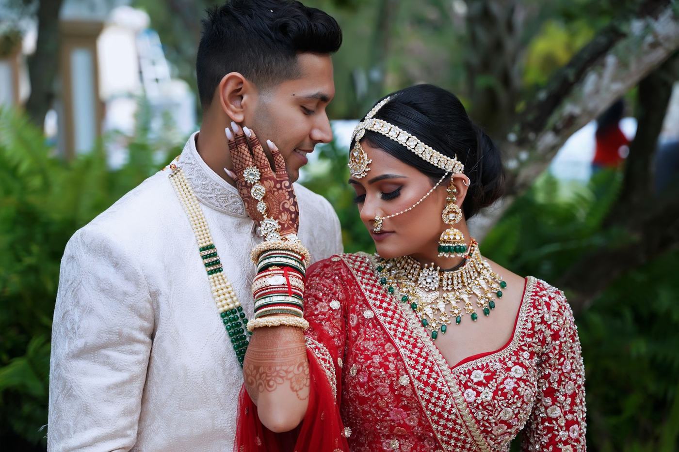 Groom in ivory touching the bride's face among tropical leaves