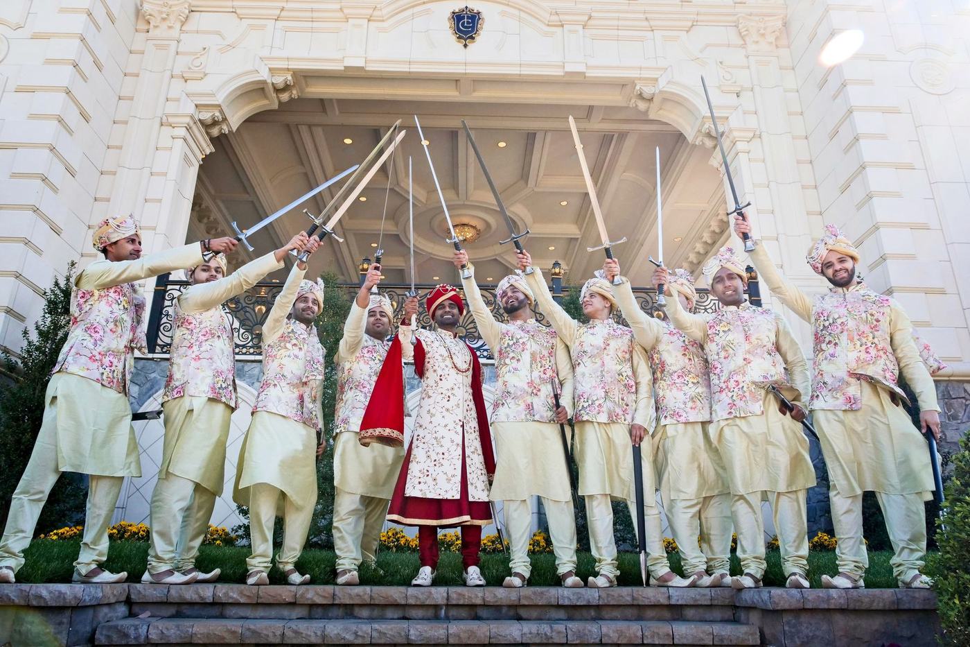 Groom and groomsmen raising swords at the estate fountain