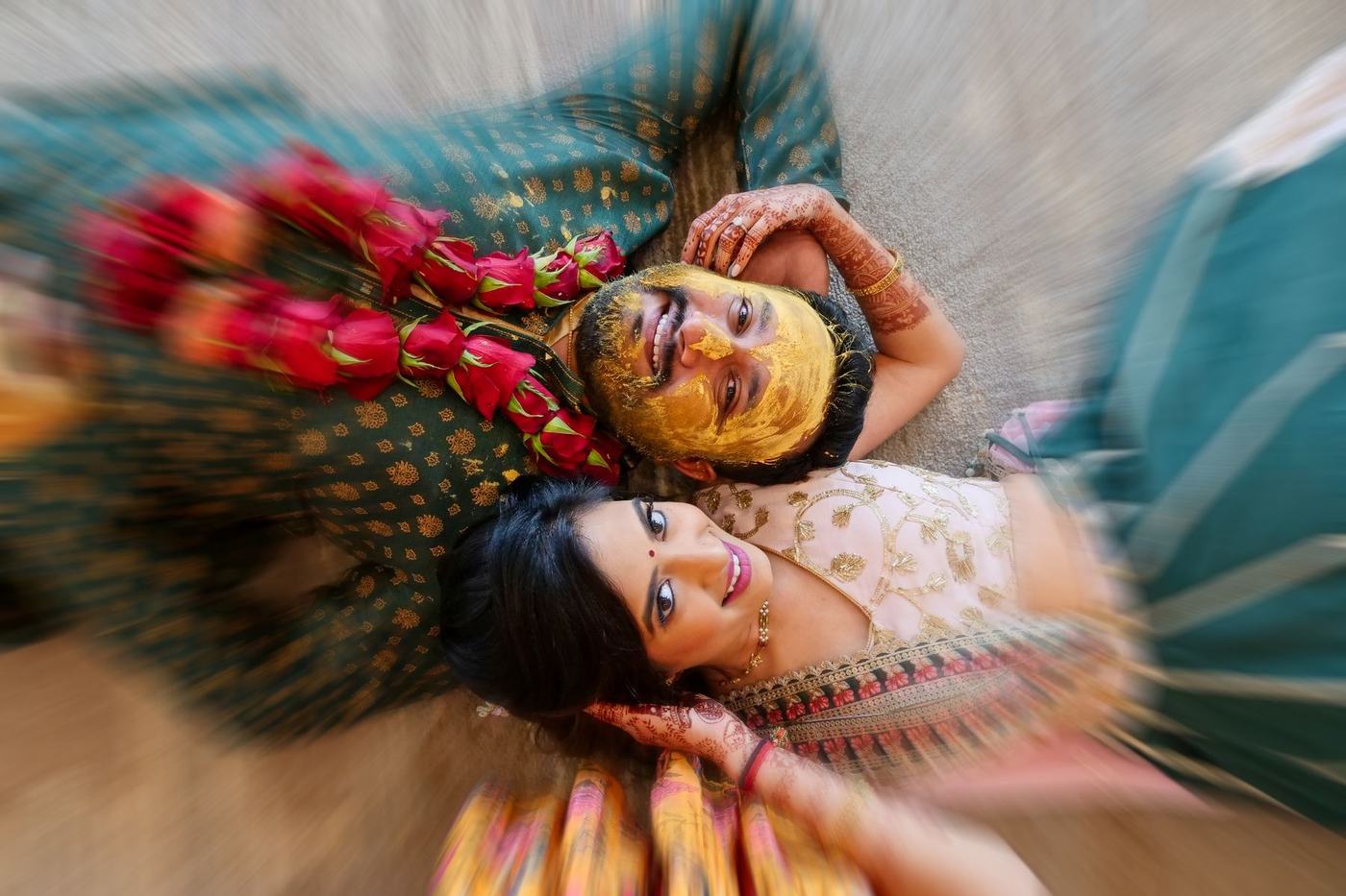 Couple lying on the floor at their haldi, seen from above in a spin of yellow and green