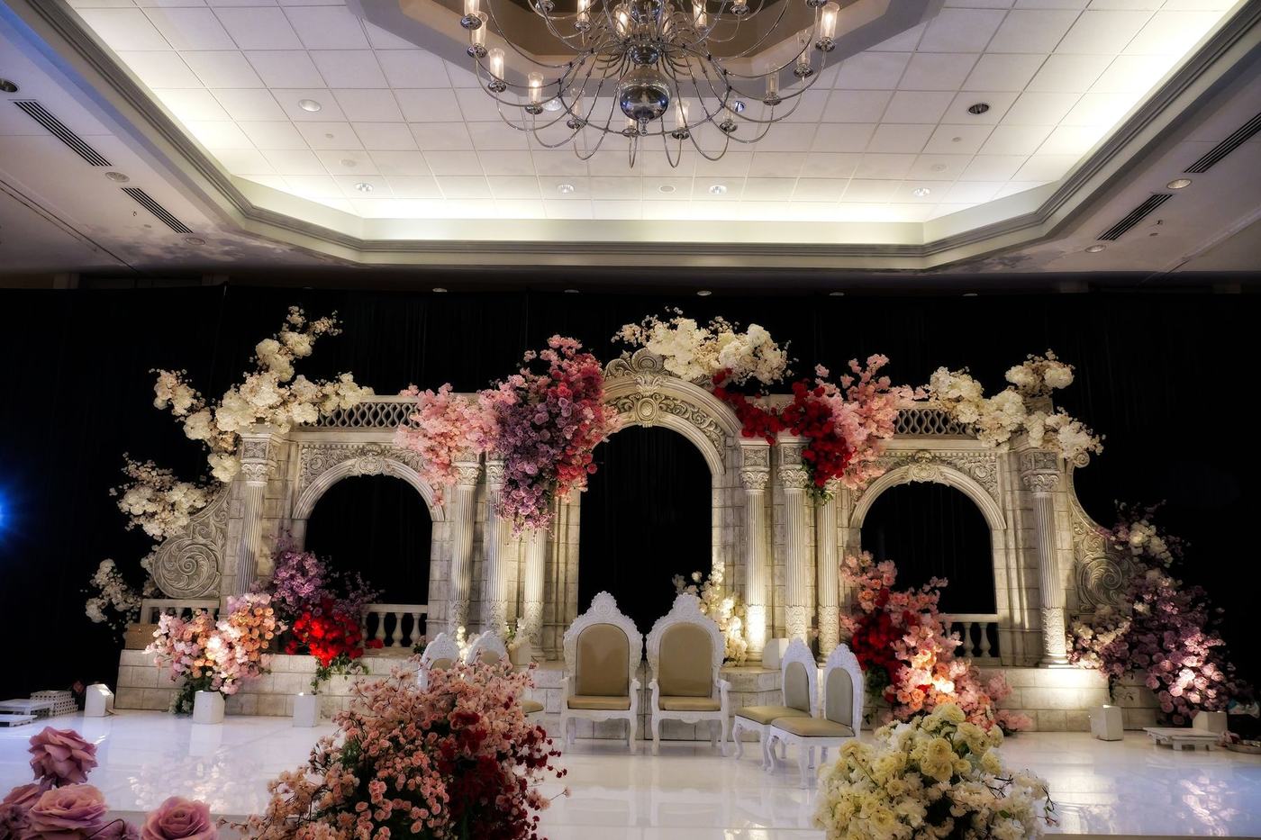 White reception stage arches dressed in blush and crimson florals